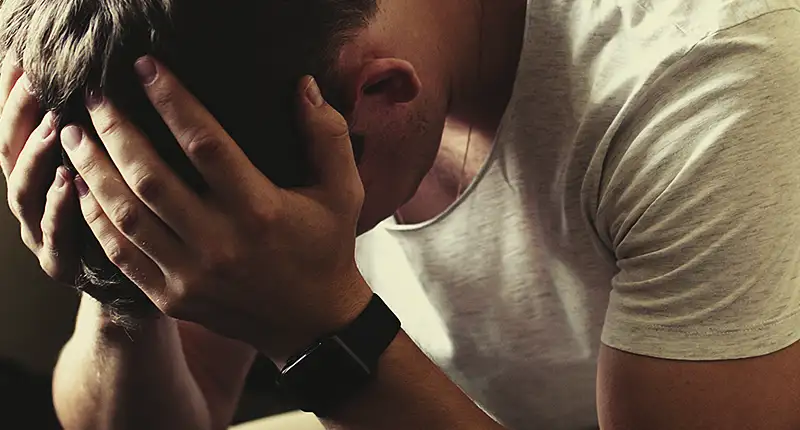 Un hombre sentado en un sofá con las manos en la cabeza, pareciendo angustiado y triste. El texto describe cómo perdió gran parte de su pensión de incapacidad debido a una revisión del INSS, pero contactando con Campmany Abogados, recuperó el 100% de su pensión a través de los tribunales.