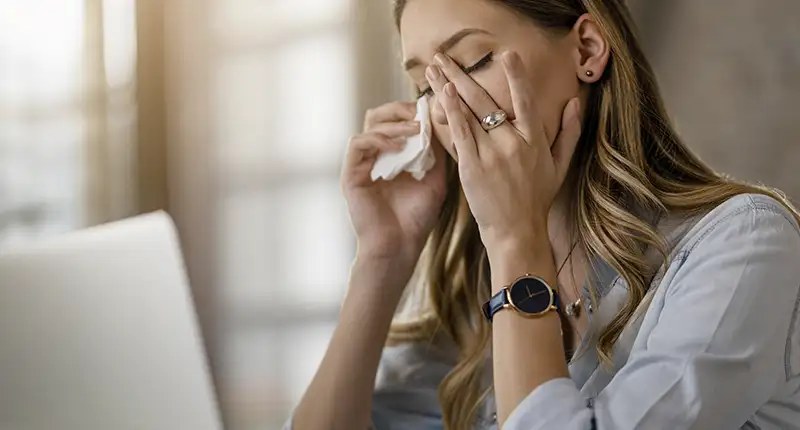 La imagen destacada del artículo muestra a una joven trabajadora que se encuentra en una situación de gran dolor y malestar debido a su migraña crónica. La mujer aparece frente a un ordenador, pero se encuentra visiblemente afectada y se está limpiando una lágrima con un pañuelo. Es una imagen que refleja la realidad de muchas personas que sufren esta enfermedad y que luchan por conseguir una incapacidad que les permita hacer frente a las limitaciones que les impone su salud.